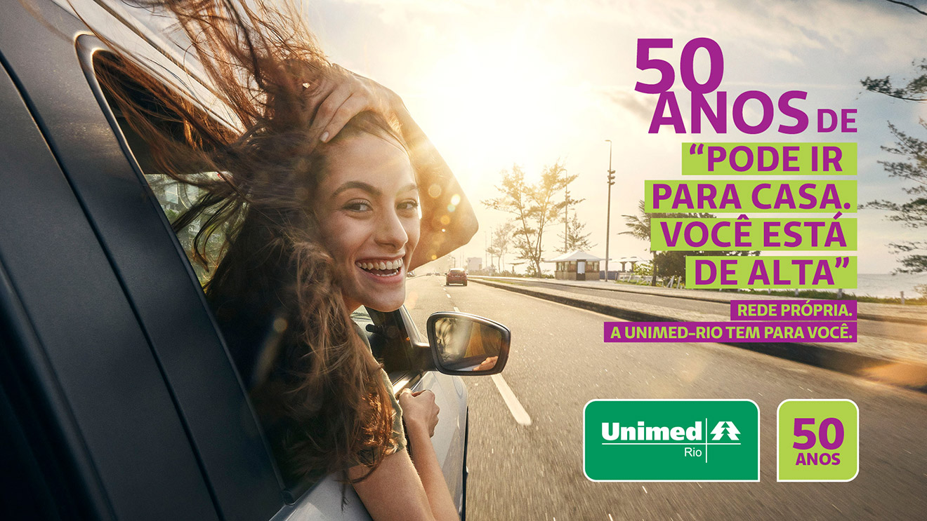 Banner Unimed-Rio com mulher jovem branca com a cabeça para fora da janela do carro olhando para trás sorrindo com o texto ao lado " 50 anos de "Pode ir para casa. Você está de alta". Rede própria. A Unimed-Rio tem para você." Com logo da Unimed-Rio e logo de 50 anos.