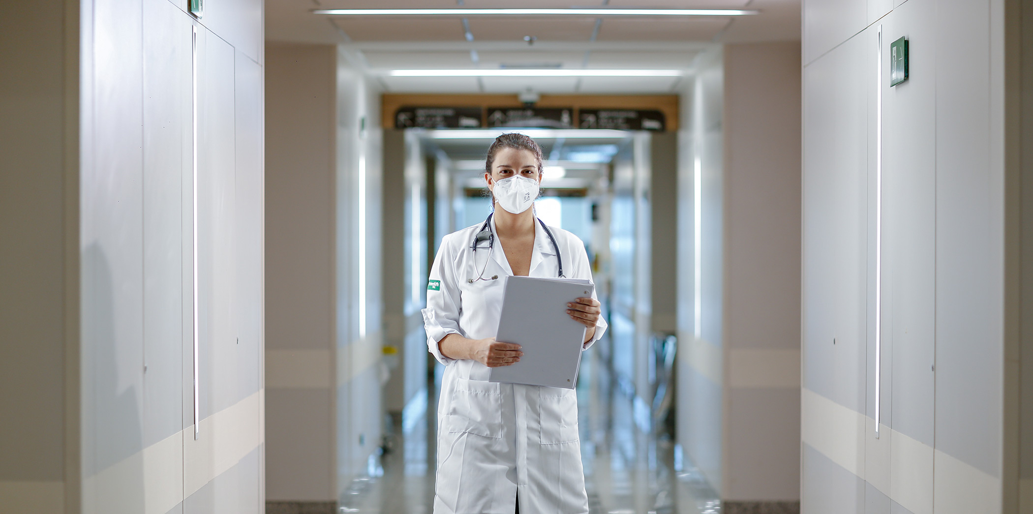 Médica da Unimed-Rio com jaleco branco em corredor de hospital.
