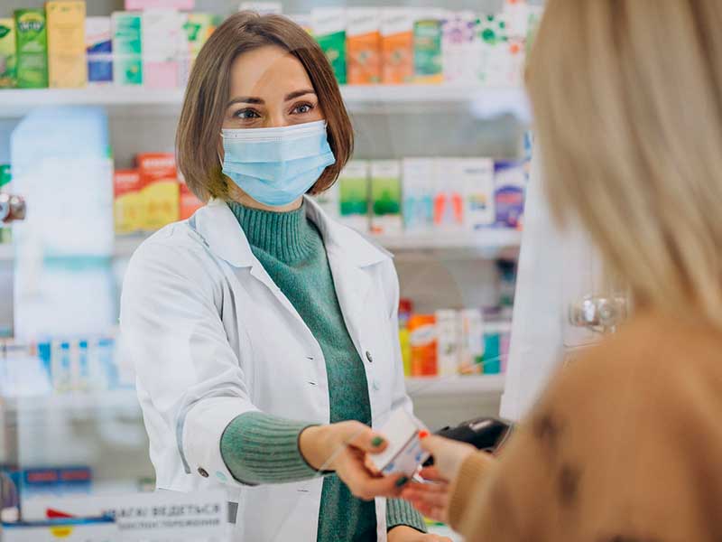 farmacêutica de jaleco entregando um remédio para uma cliente de costas