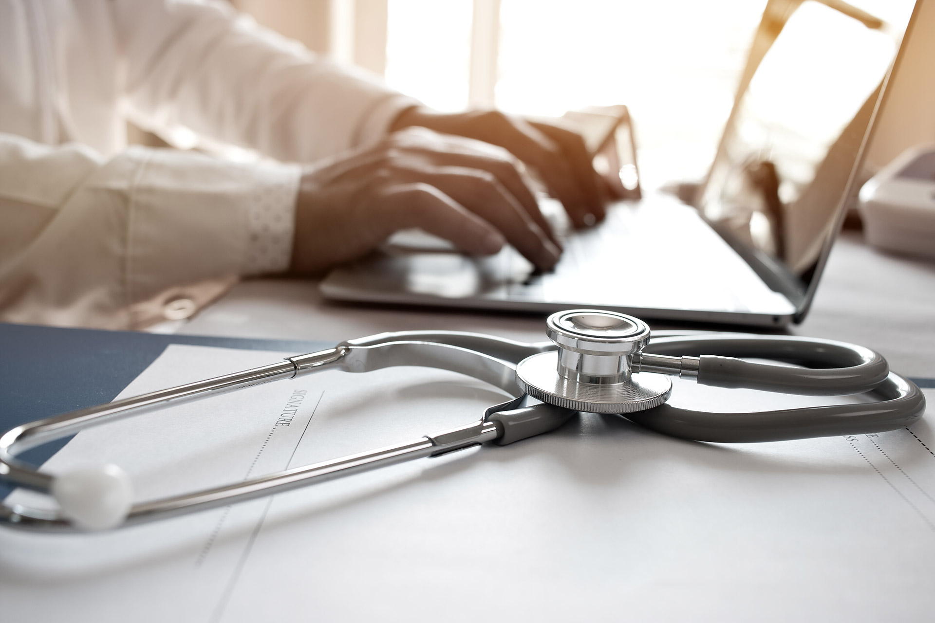 Médico utilizando laptop com o estetoscópio ao lado
