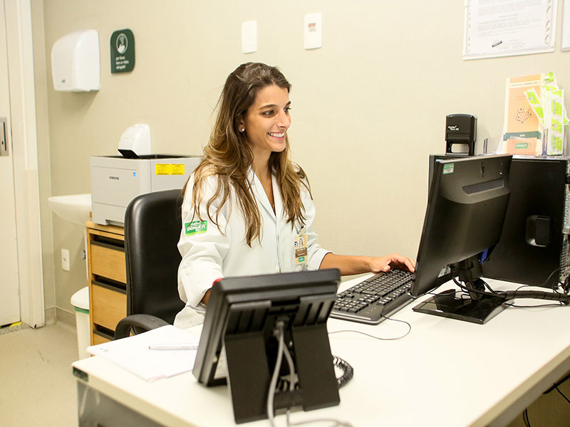 Médica utilizando o computador em sua mesa de atendimento.